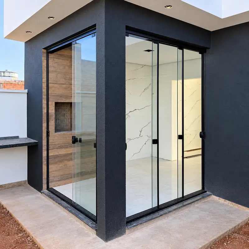Canto envidraçado com portas de vidro temperado e perfil preto numa casa de fachada escura